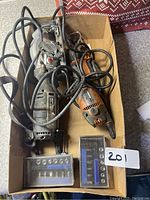 Power saws and ratchet sets in cardboard box with visible cords and tool marks.