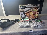 Full lot with Gotham Steel electric smoke-less grill in box, handheld vacuum on left, three sealed packs of white decorative string lights in front.