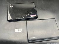 Top view of two closed laptops on black surface, one HP with textured lid and circular pattern in upper left, one Toshiba with plain matte lid with visible scratches.