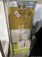 Stack of boxed Hampton Bay chandeliers: top box labeled 5-Light Westwood Chandelier with oil-rubbed bronze finish and frosted white glass shades, middle and bottom boxes are 3-Light Chester chandeliers with multi-turn finish and glass shades. Boxes show wear and damage.