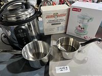 Photo showing all items in lot: Crock Pot pressure cooker, two saucepans, Jolly Party napkins box, DASH shaved ice maker box.