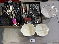 Image of assorted kitchen utensils in trays, including forks, spoons, spatulas, tongs, and ladle. Also shows three ceramic bowls with lids.