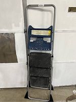 Full view of folded metal and plastic Cosco step ladder with black steps and blue platform showing general condition and design