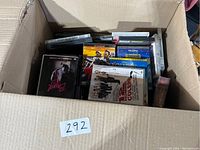 Top view of a box filled with assorted DVD movies showing various titles and cases stacked inside.