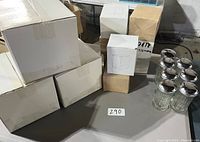 Photo of multiple unopened cardboard boxes containing new restaurant equipment items, including a small boxed napkin holder and straw dispenser.