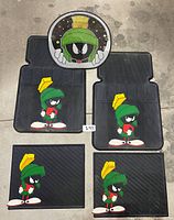 Set of four black rubber car mats featuring Marvin The Martian graphics laid out on floor for display.