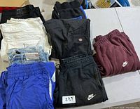 Nine pieces of men's jeans and sweatpants placed on table, multiple brands and colors visible, labeled with lot number 237.