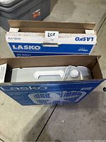 Photo of the tops of two packed Lasko box fans in their original boxes showing the white fan casing and handles.
