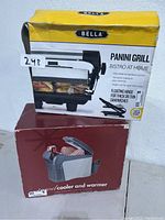 Two boxed kitchen appliances: Bella Panini Grill box on top and a travel cooler and warmer box beneath.