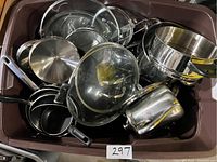 Overview of various pots and pans including stainless steel cookware and glass lids inside a plastic tub.