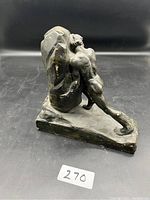 Side view of the dark bronze sculpture showing the muscular man pushing a rock, mounted on a base.