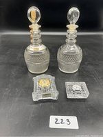 Two glass decanter bottles with stoppers and two small glass clocks on black surface.
