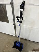 Snow Joe cordless electric snow shovel standing upright, telescoping handle extended with secondary grip visible.