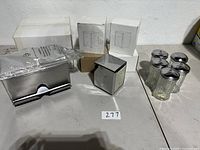 Full view of all items in the lot including napkin holder, straw dispenser, glass sugar containers and boxes on a table.