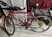 Side view of the red Trek Antelope 820 mountain bike leaning against a cabinet. Shows the whole bike with flat tires and some dust.
