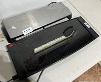 Two electric food warming trays, one stainless steel and one black glass top, with power cords, placed on a table.