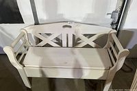 Front view of white wooden bench showing backrest with cutout pattern, armrests, and hinged seat.