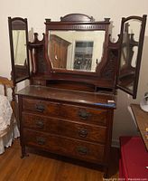 Full view of antique dresser with three folding mirrors attached on top, ornate carved wood details on top and sides, five drawers with metal handles, missing one drawer.
