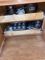 Photo showing two wooden drawers containing various pots, pans, muffin tin, and bowls.