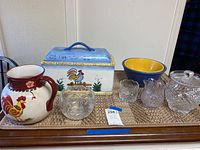 Wide view of all items including ceramic breadbox, pitcher, bowls, and cut glassware on a wooden tray.