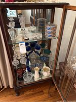 Wide-angle photo of glass display cabinet with multiple shelves filled with various glassware and porcelain items, showing overall lot contents.