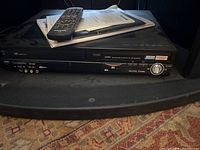 Panasonic VHS DVD player showing front-facing controls and discs tray, with remote and user manuals on top of Sony TV stand