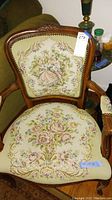 Close-up photo of wood frame chair with detailed tapestry upholstery showing classical romantic scene and floral motifs.