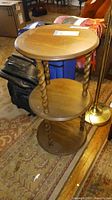 Wooden 3-tier round table with twisted columns and circular shelves on a patterned rug with other furniture items.