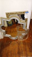 Three items: two ornately framed decorative mirrors and one rectangular picture frame grouped together on wooden floor.
