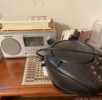 Wide photo showing Sangean radio, beige Sony radio on top, and Onn radio at right edge.