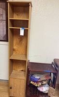 Narrow wooden shelf unit and rolling cart side by side against a wall