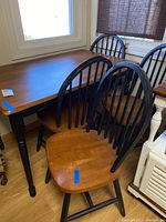 Photo showing the rectangular wooden breakfast table with warm brown finish top and black legs, along with four chairs with wooden seats and black vertical slat backs.