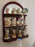 Full view of all porcelain Tweety Bird figurines displayed on a three-shelf wooden mirror-backed rack, showing different themed poses and costumes representing months of the calendar.