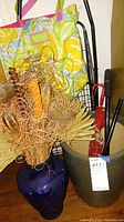 Photo of the blue glass vase with dried floral arrangement, ceramic umbrella holder with umbrellas, and black metal cart with wheels grouped together.