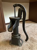 Side view of antique cast iron water hand pump showing the spout, lever handle and base.