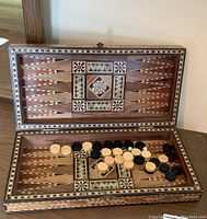 Open backgammon board showing mosaic inlay and black and white playing pieces with dice inside.