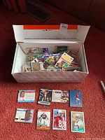 Shoebox full of assorted sports cards with some football cards laid out in front for detail showing front and back sides