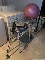 Walker with padded handles and 2 wheels, commode with extra pot on top, and walking sticks in front of washer and dryer.