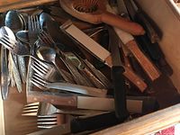 View inside drawer showing mixed flatware including forks and spoons with ornate handles and some serving utensils