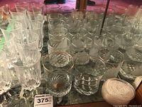 Photo showing multiple drinking glasses including cut pattern and plain glasses, and some plastic coasters on right.