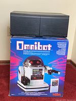 Boxed Omnibot robot stacked under black plastic organizer