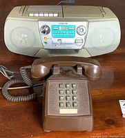 Vintage brown push-button landline telephone and Sony portable radio/CD player on wooden surface.