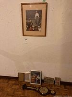 Overall view showing the Norman Rockwell print hanging on the wall, with three framed photos, the stone art, and the wall-mount barometer placed on the floor beneath it.