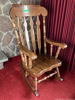 Side view of the oversized solid wood rocking chair, showing carved armrest and spindle detail with visible wood grain and scratches.