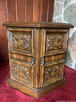 Side view of vintage hexagonal wooden side table showing detailed carved door panels and metal handles.