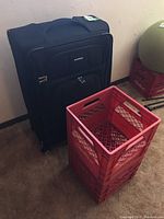 Black Samsonite suitcase standing upright with two red plastic milk crates stacked in front of it.