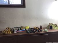 Power unit, two train controllers, yellow extension cord, and five rolling stock pieces laid on a wooden surface against a white wall.