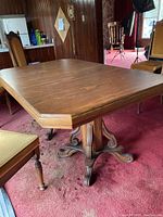 Side angled view of vintage solid wood dining table showing pedestal base and scratched top surface