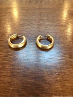 Pair of small 14K gold hoop earrings displayed side by side on wooden surface.