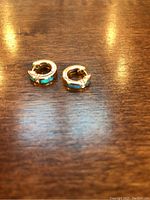 Pair of small gold hoop earrings with opal inlays and diamonds, front view on wood table